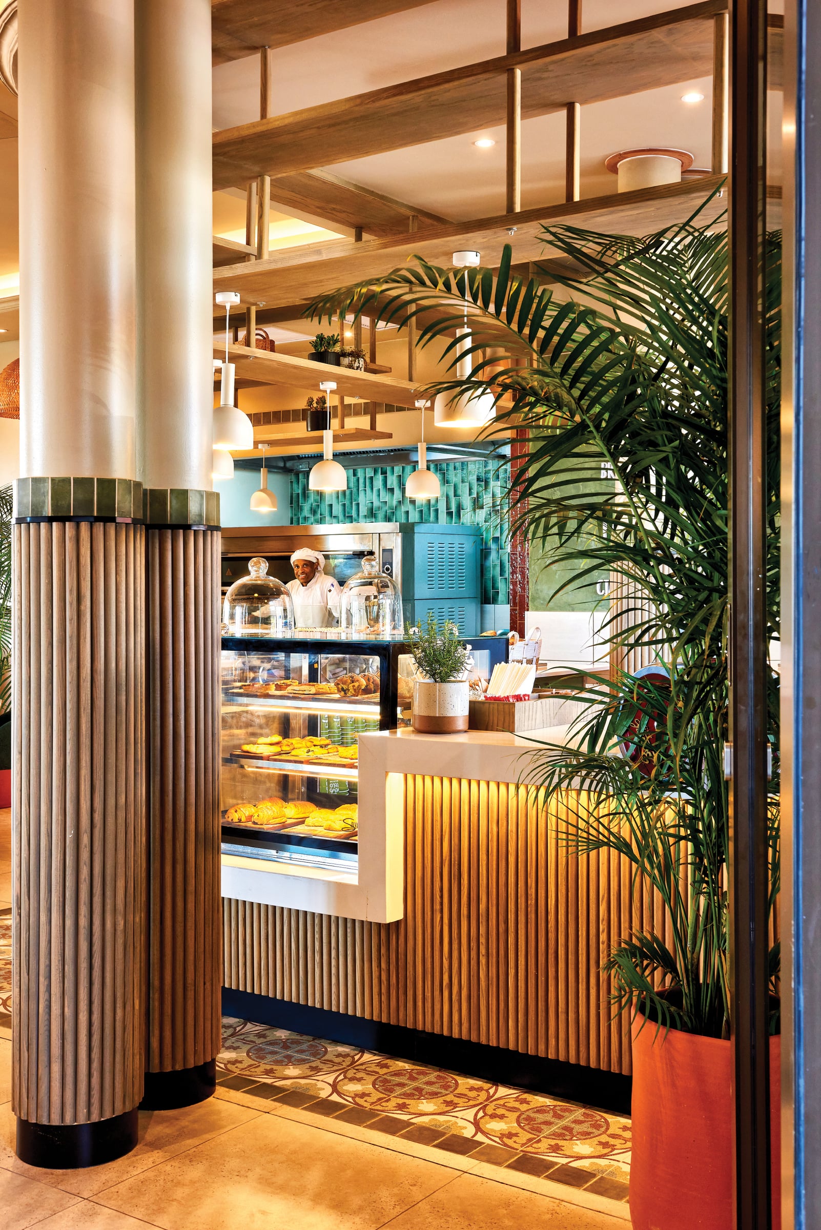 Inside the bakery, a baker at the pastry counter surrounded by warm wood and greenery