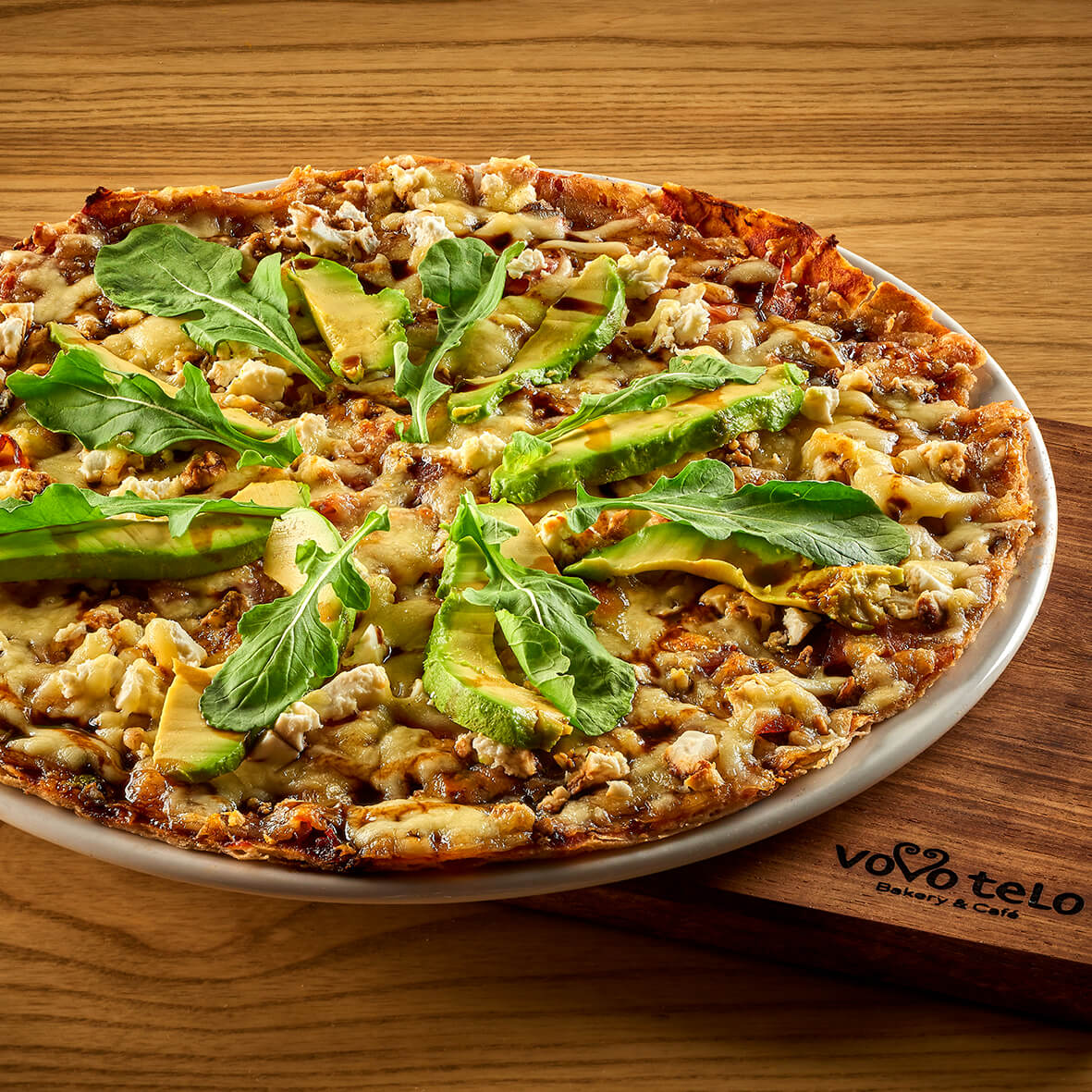 Thin-crust pizza topped with avocado and rocket on a Vovo Telo board